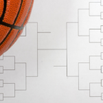 An orange basketball resting on a crisp white single-elimination Tournament Bracket sheet on a rustic wooden tabletop.