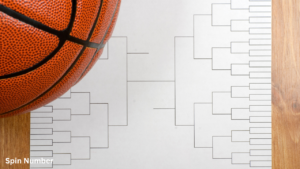 An orange basketball resting on a crisp white single-elimination Tournament Bracket sheet on a rustic wooden tabletop.