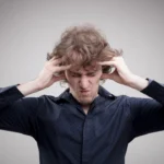 A man clutching his head in frustration with his eyes tightly shut, demonstrating the intense stress of mental looping before learning How to Stop Overthinking.