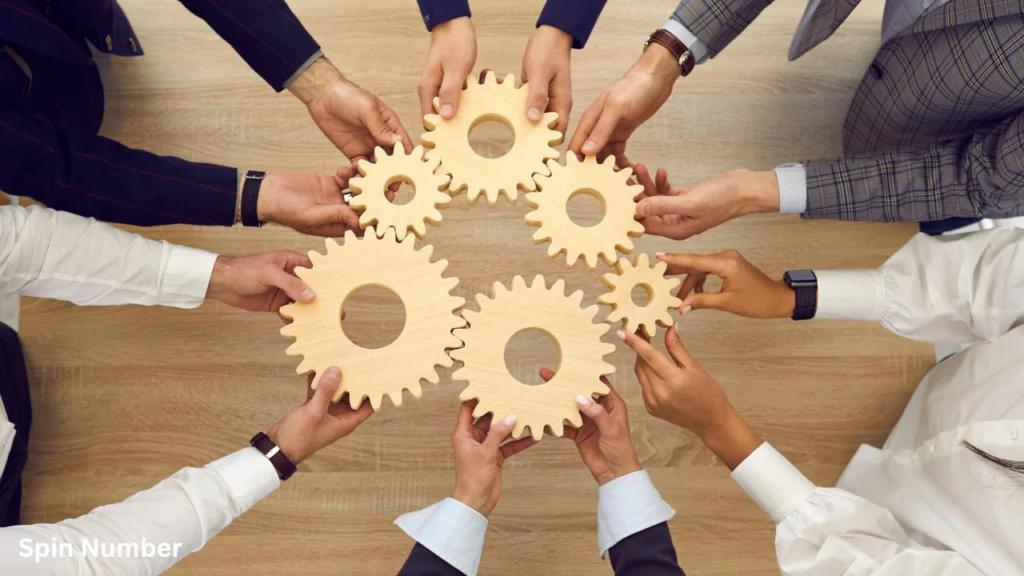 An overhead view of a professional team interlocking a circle of wooden gears on a conference table during corporate Team Building Activities.