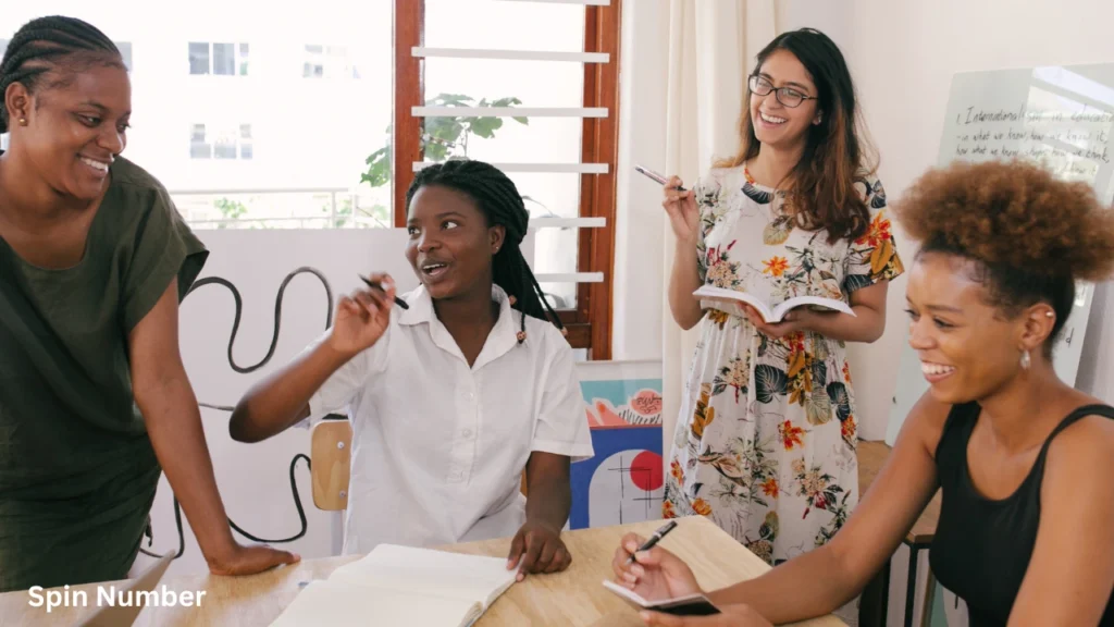 Four creative women collaborating, writing in notebooks, and smiling together at a workshop table, an ideal setting for engaging ice breaker questions.