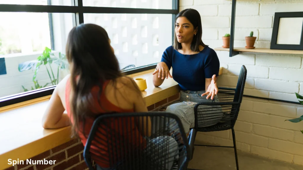 Two young women sitting at a cafe table by a large window, engaging in deep conversation over deep Never Have I Ever Questions.