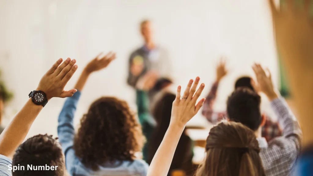 Multiple students raising their hands from their desks during a seminar with a blurred teacher in the background, responding to interactive ice breaker questions.