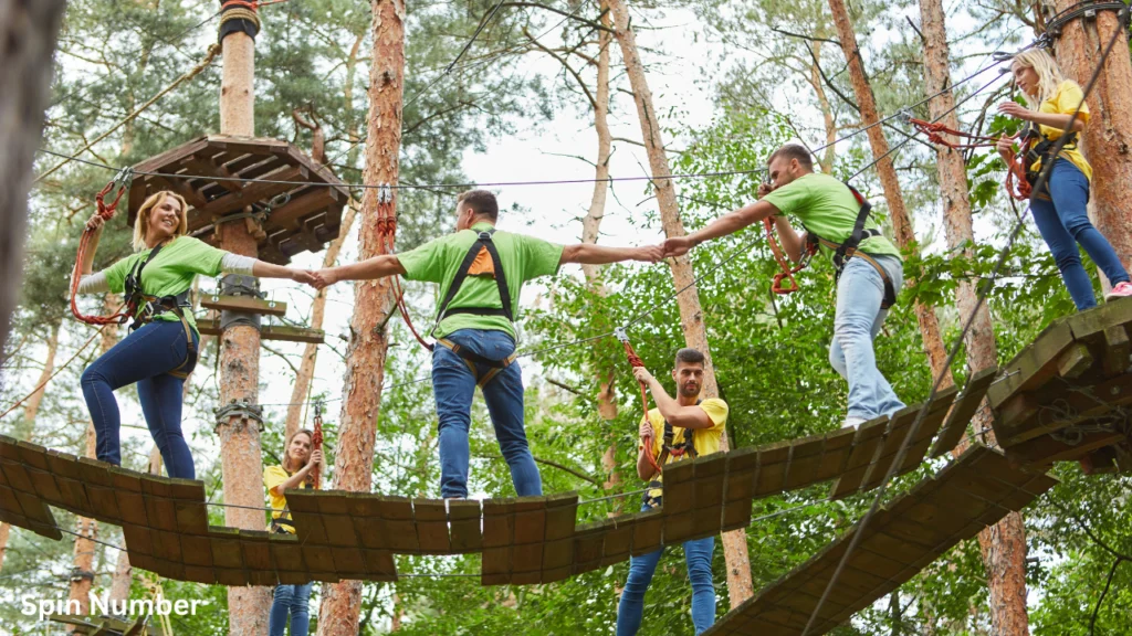 Coworkers wearing matching t-shirts holding hands to support one another on an outdoor ropes course bridge during Team Building Activities.