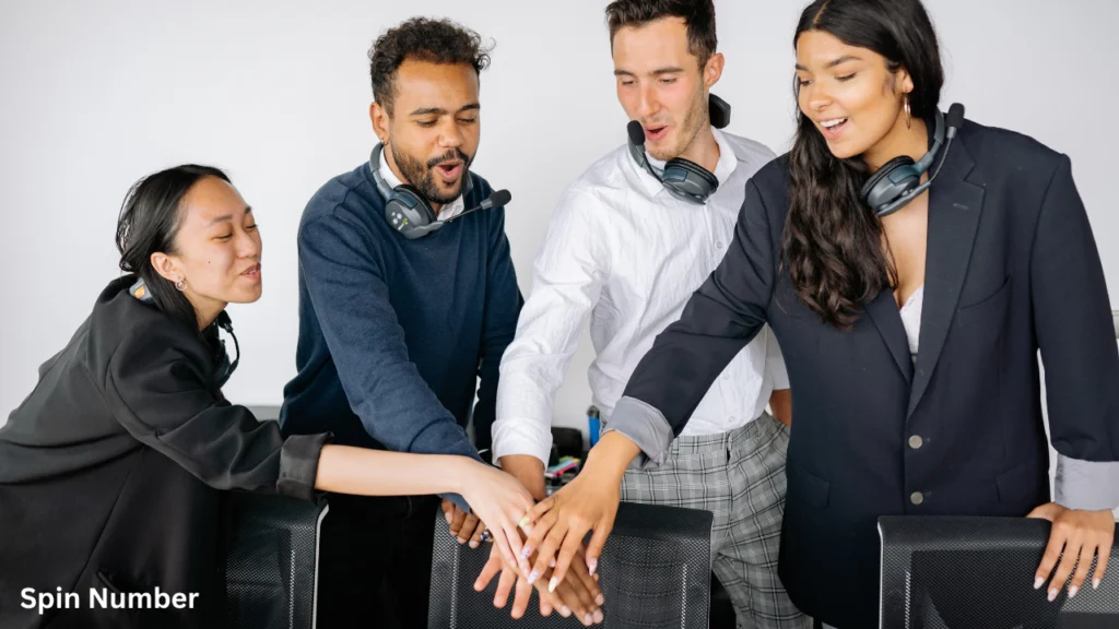 A group of four diverse call center professionals in business casual clothing putting their hands together in a huddle, showcasing unity after being paired by a random team generator
