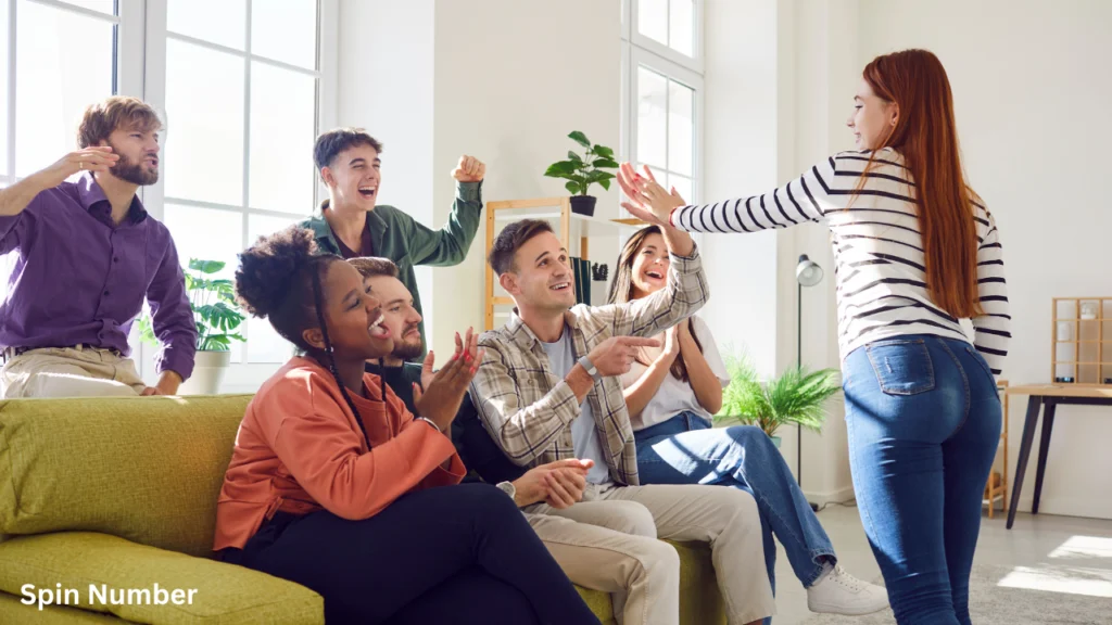 A group of friends cheering on a living room sofa while a woman acts out clues during charades, a staple of classic Party Games for Adults.